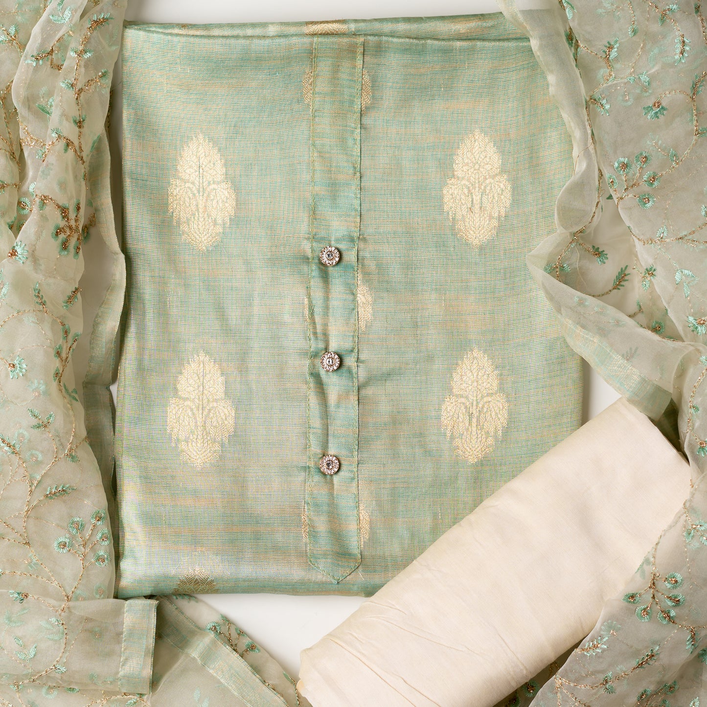 An elegantly crafted Tissue Silk Party wear dress material. A set best suited to gift bride to be or your loved on your anniversary. Tissue silk top with golden color embossed designs, it has show buttons in neck area, also golden color borders in side. Tissue silk dupatta with embroidery work with the same color thread of top and also golden color threads. Cream color cotton silk bottom.