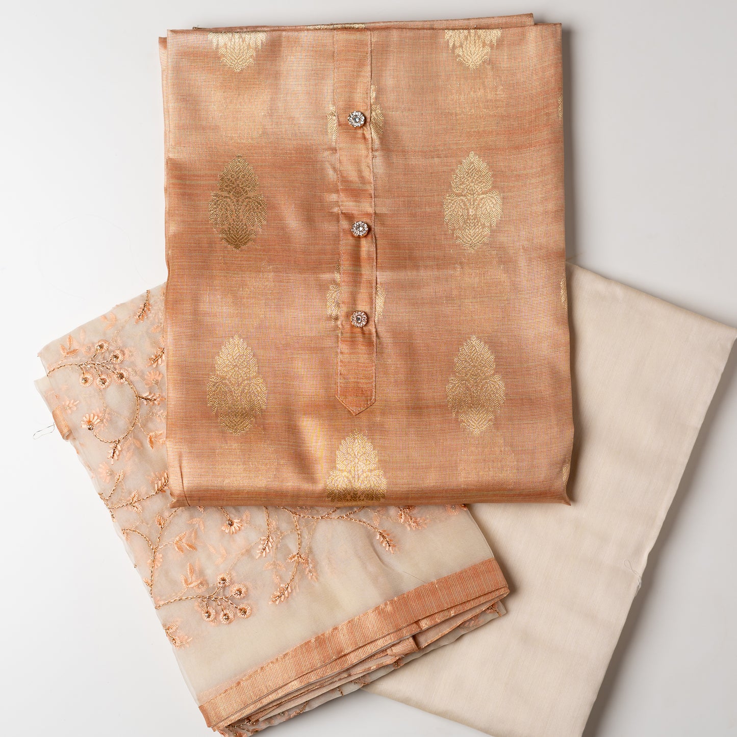 An elegantly crafted Tissue Silk Party wear dress material. A set best suited to gift bride to be or your loved on your anniversary. Tissue silk top with golden color embossed designs, it has show buttons in neck area, also golden color borders in side. Tissue silk dupatta with embroidery work with the same color thread of top and also golden color threads. Cream color cotton silk bottom.