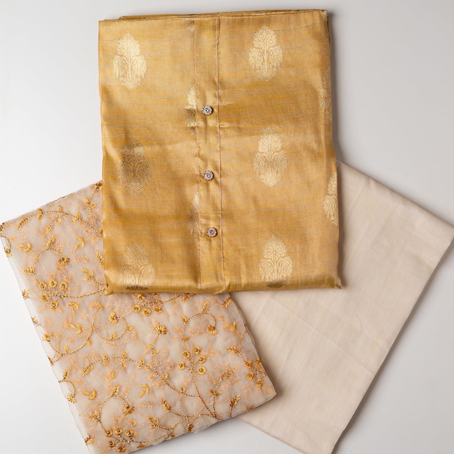 An elegantly crafted Tissue Silk Party wear dress material. A set best suited to gift bride to be or your loved on your anniversary. Tissue silk top with golden color embossed designs, it has show buttons in neck area, also golden color borders in side. Silk dupatta with embroidery work with the same color thread of top and also golden color threads. Cream color cotton silk bottom.