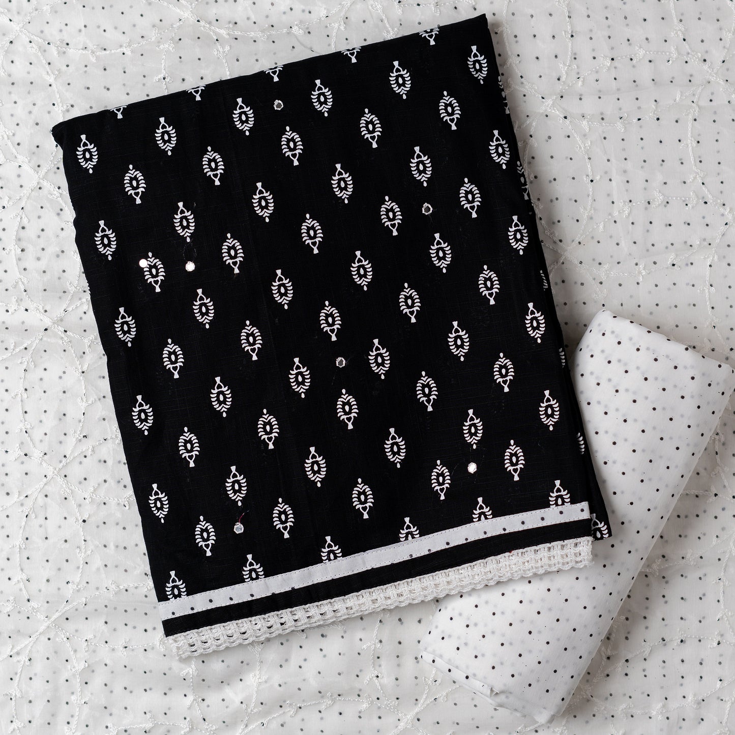 Cotton black color dress material with beautiful print design in white color on top, mirror work. It has white color lace on the borders. Chiffon dupatta with embroidery work in white color and black dotted prints. Cotton white color bottom with black dots.