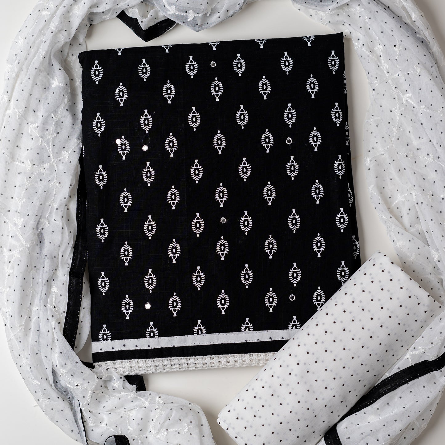 Cotton black color dress material with beautiful print design in white color on top, mirror work. It has white color lace on the borders. Chiffon dupatta with embroidery work in white color and black dotted prints. Cotton white color bottom with black dots.