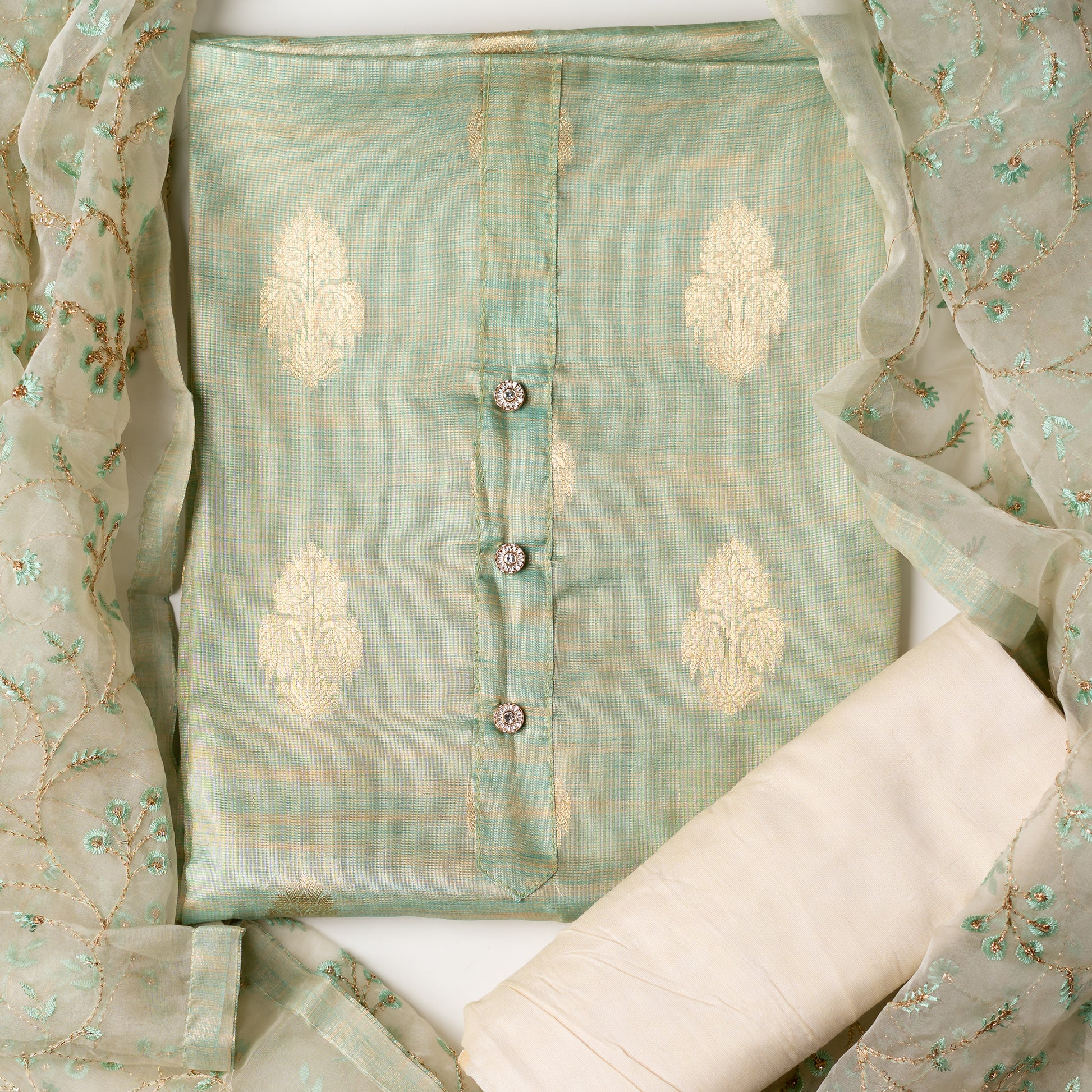 An elegantly crafted Tissue Silk Party wear dress material. A set best suited to gift bride to be or your loved on your anniversary. Tissue silk top with golden color embossed designs, it has show buttons in neck area, also golden color borders in side. Tissue silk dupatta with embroidery work with the same color thread of top and also golden color threads. Cream color cotton silk bottom.