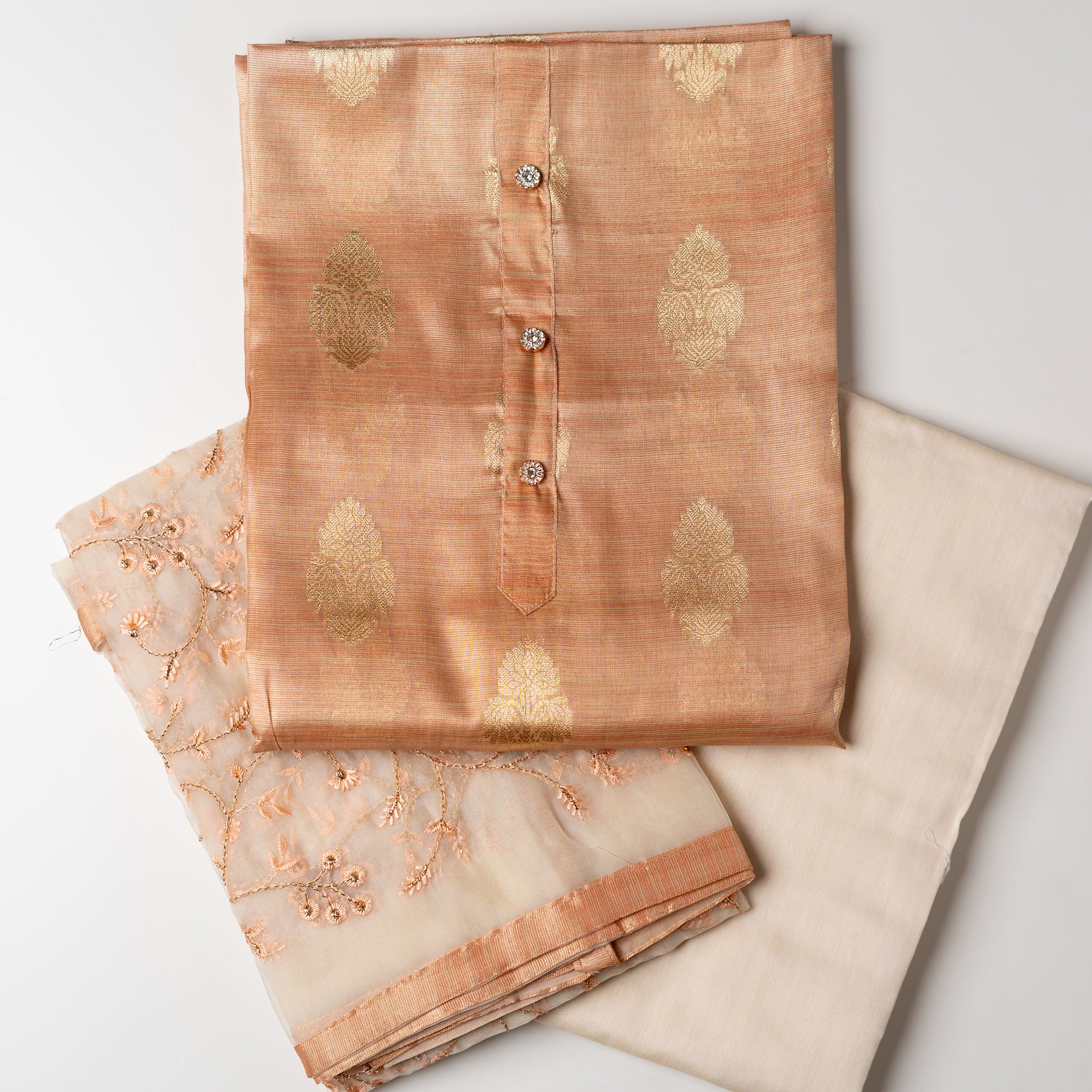 An elegantly crafted Tissue Silk Party wear dress material. A set best suited to gift bride to be or your loved on your anniversary. Tissue silk top with golden color embossed designs, it has show buttons in neck area, also golden color borders in side. Tissue silk dupatta with embroidery work with the same color thread of top and also golden color threads. Cream color cotton silk bottom.