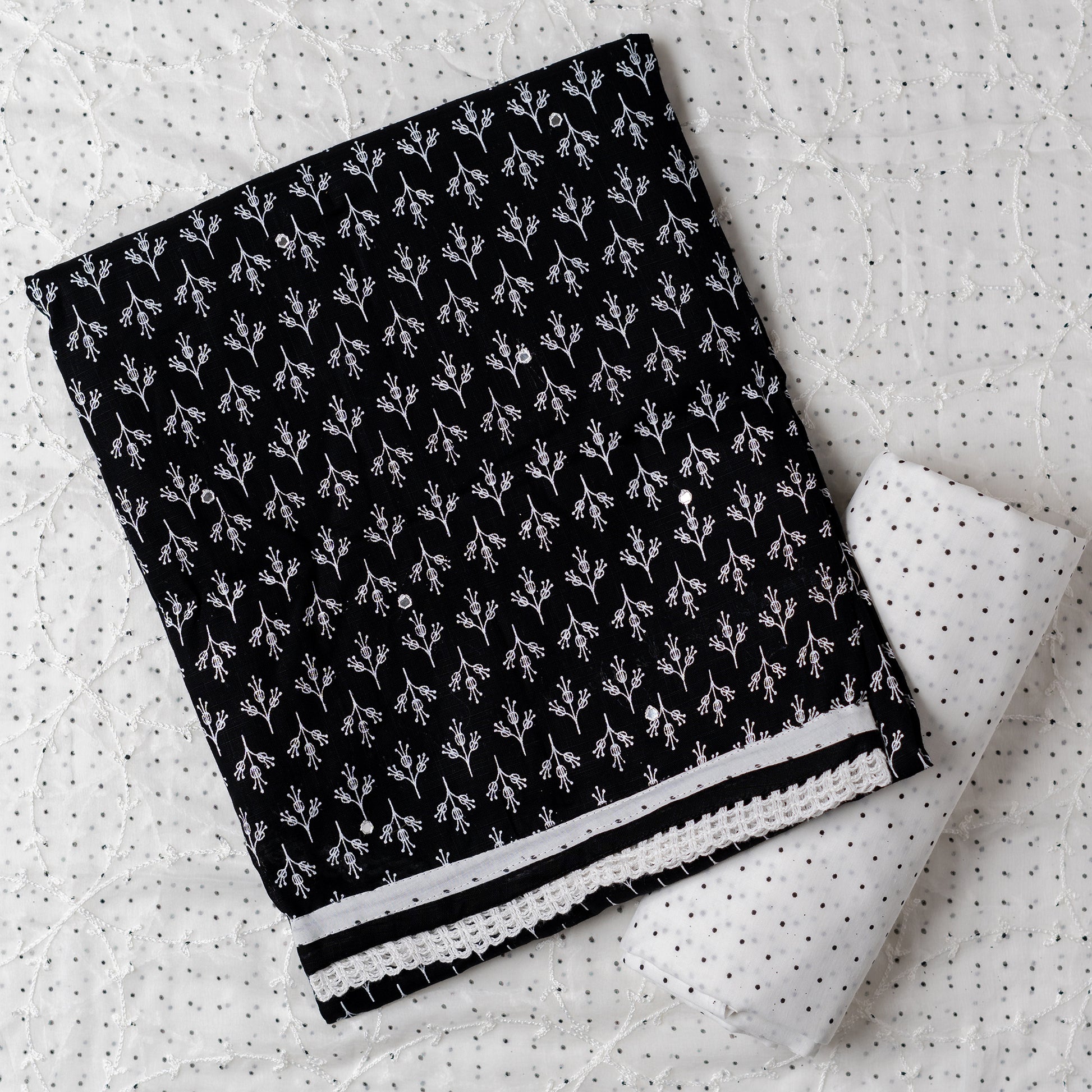 Cotton black color dress material with beautiful print design in white color on top, mirror work. It has white color lace on the borders. Chiffon dupatta with embroidery work in white color and black dotted prints. Cotton white color bottom with black dots.