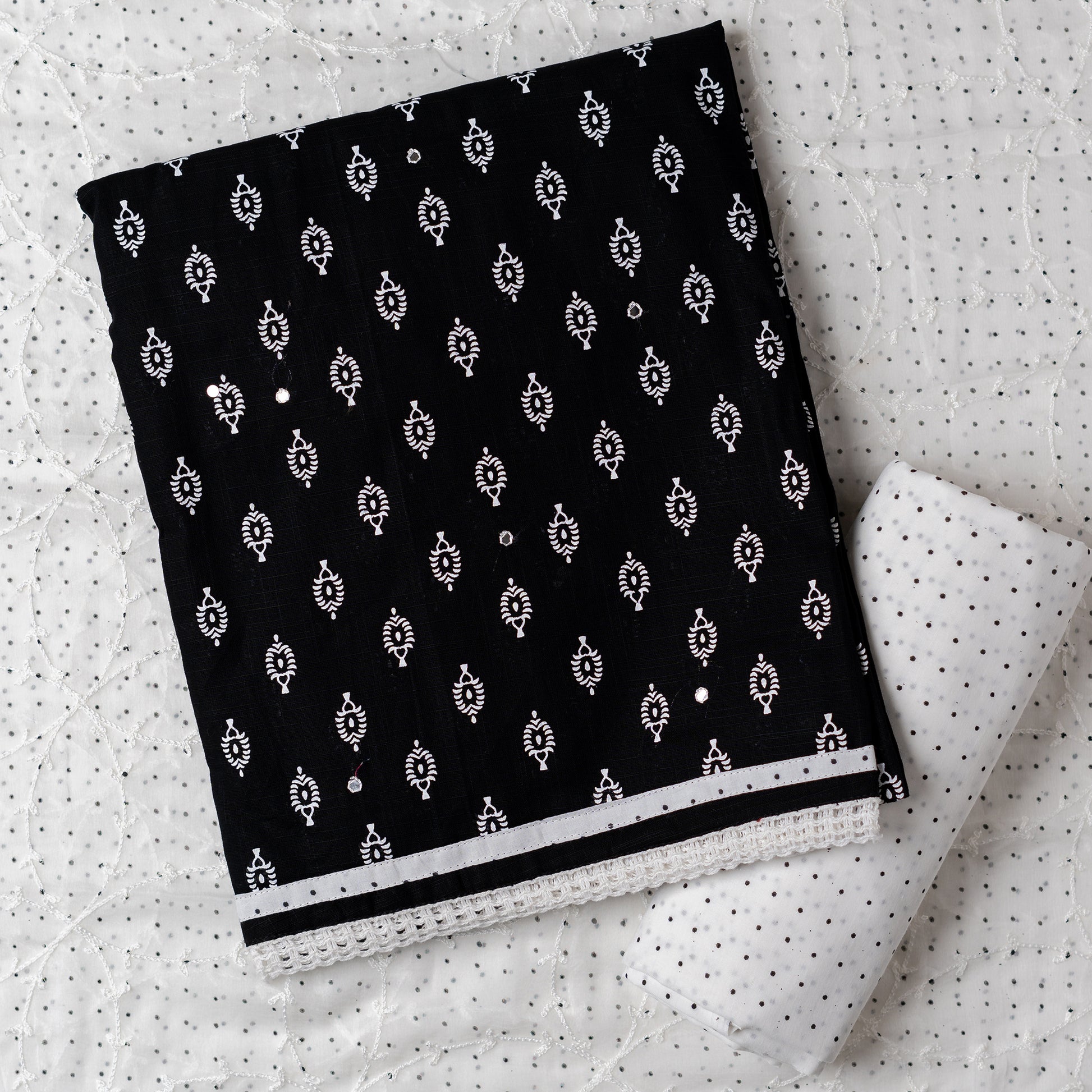 Cotton black color dress material with beautiful print design in white color on top, mirror work. It has white color lace on the borders. Chiffon dupatta with embroidery work in white color and black dotted prints. Cotton white color bottom with black dots.