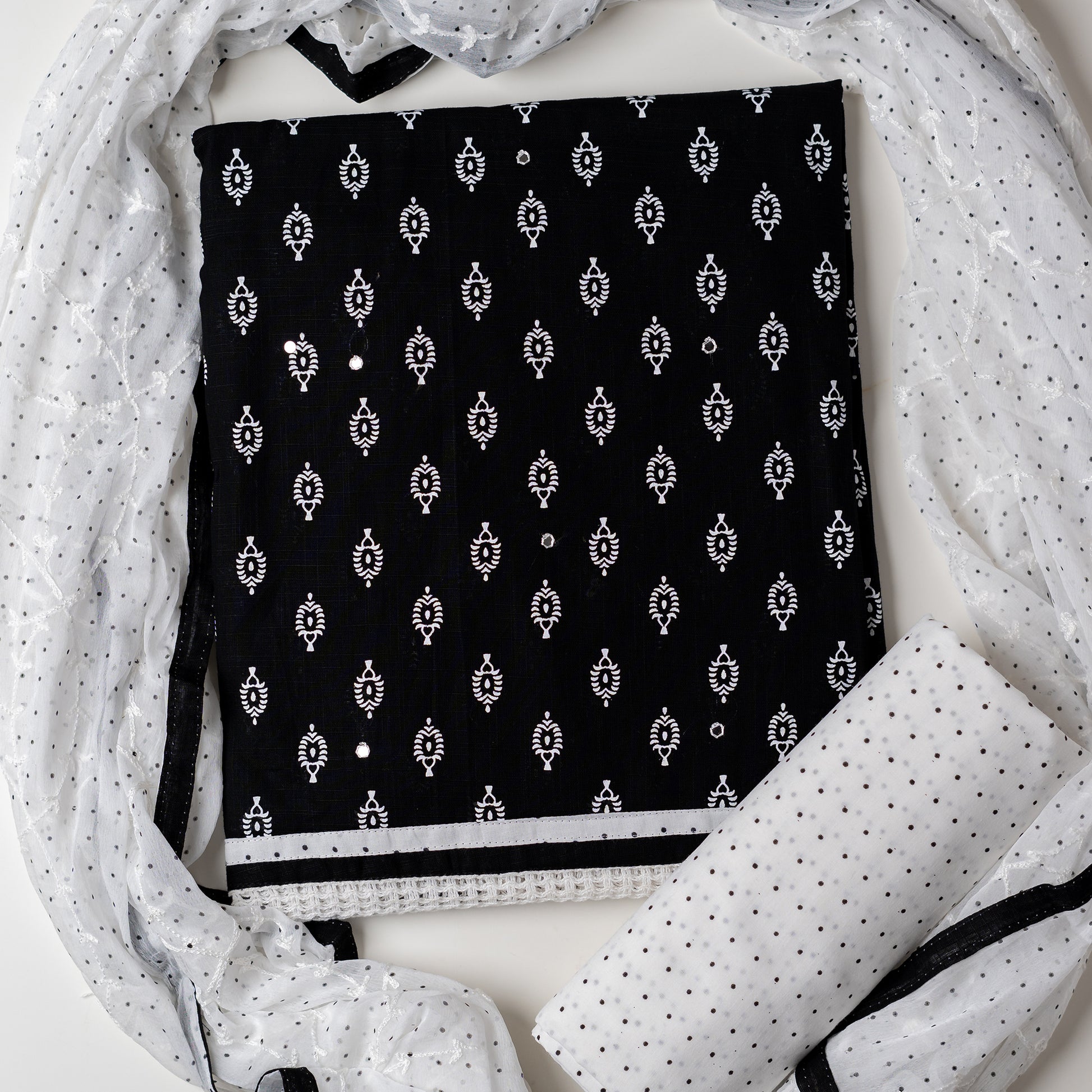 Cotton black color dress material with beautiful print design in white color on top, mirror work. It has white color lace on the borders. Chiffon dupatta with embroidery work in white color and black dotted prints. Cotton white color bottom with black dots.