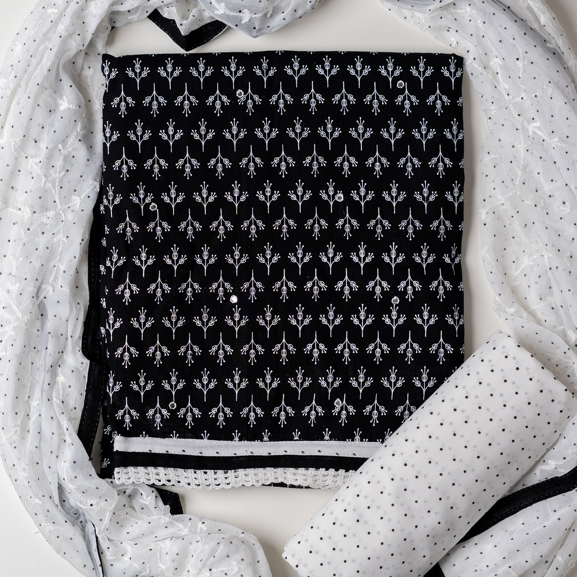 Cotton black color dress material with beautiful print design in white color on top, mirror work. It has white color lace on the borders. Chiffon dupatta with embroidery work in white color and black dotted prints. Cotton white color bottom with black dots.