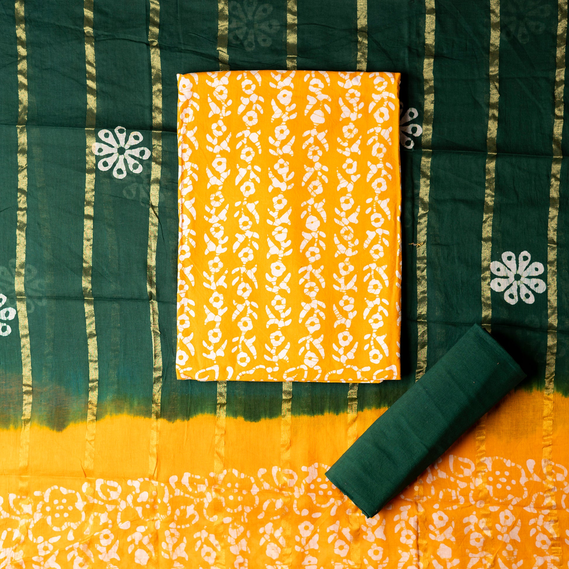 Yellow color cotton wax batik dress material with white prints, cotton green color bottom with batik prints. Cotton green and yellow color dupatta with golden color lines in between and wax batik prints
