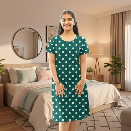 A woman stands in a modern living room wearing a short-sleeve green dress with white polka dots. 