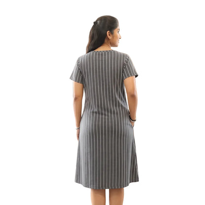 A woman stands with her back to the camera wearing a short-sleeve gray dress with thin white vertical stripes with hand in right side pocket