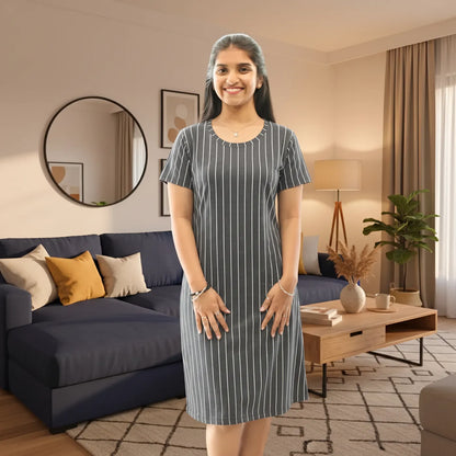 A woman stands in a modern living room wearing a short-sleeve, knee-length dress with thin vertical white pinstripes on a slate blue-gray background. 