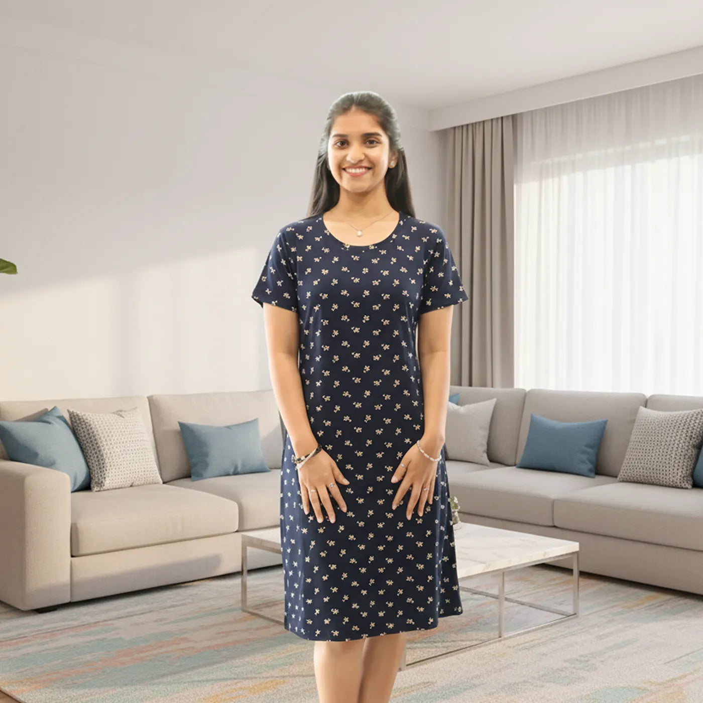 A woman stands in a modern living room wearing a navy blue cotton knee length short nighty  with a small white floral pattern. 