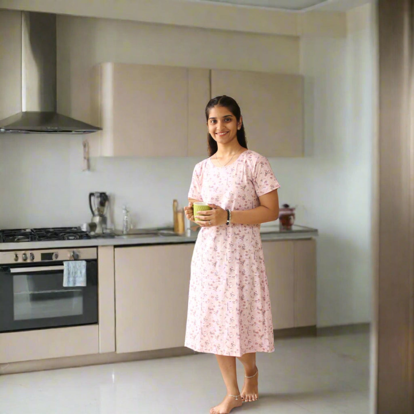 women holding a coffee mug and standing in a kitchen wearing light pink color cotton short nighty