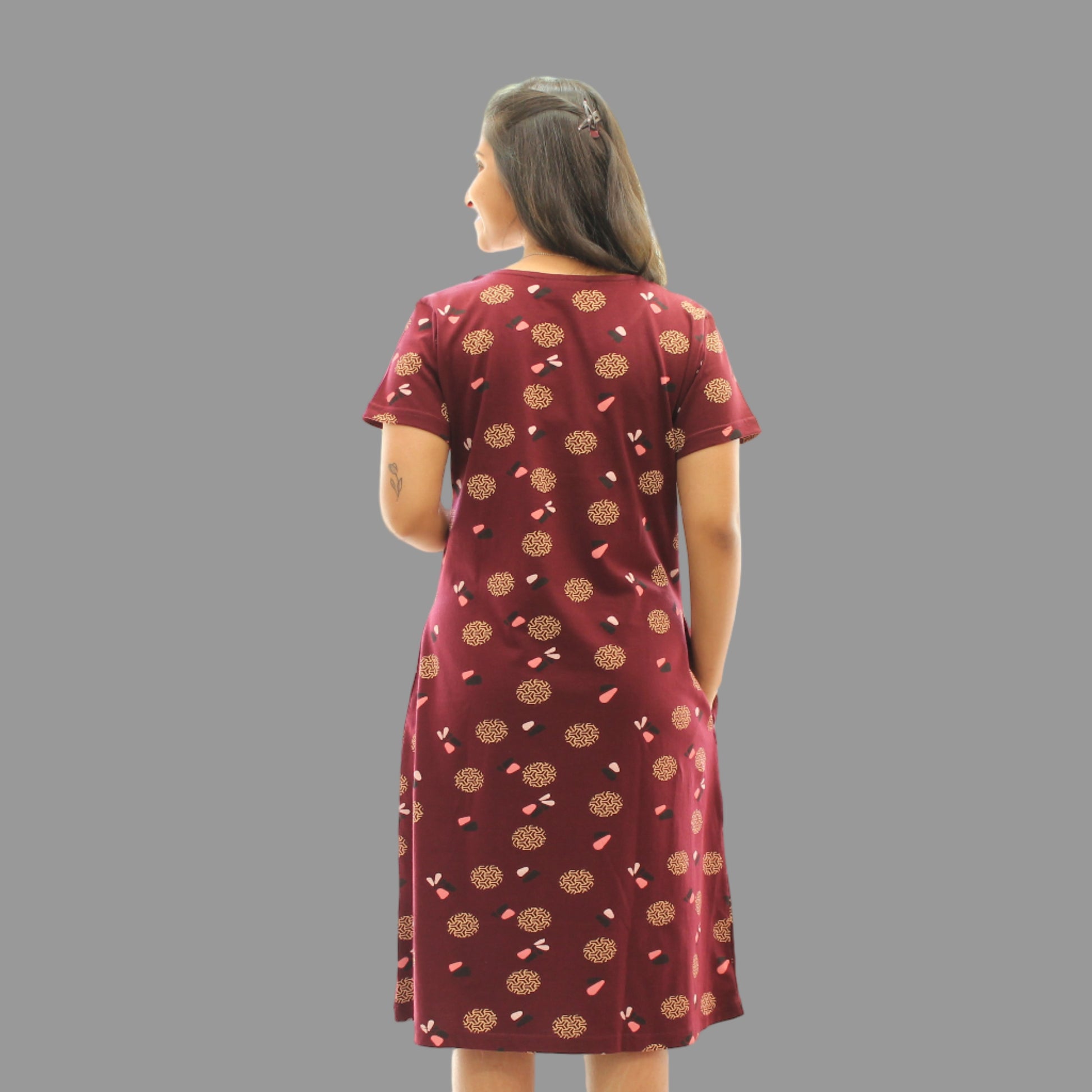 women wearing dark maroon cotton knee length short nighty with all over print design and standing backwards it has a pocket.