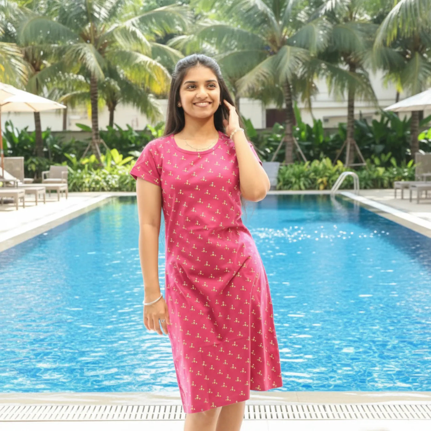 Woman in a red knee length dress standing by a pool with palm trees in the background