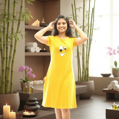 Woman wearing a yellow dress with a smiley face design in a room with plants and candles.
