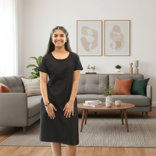 Woman in a black dress standing in a living room with gray sofa and wooden coffee table.