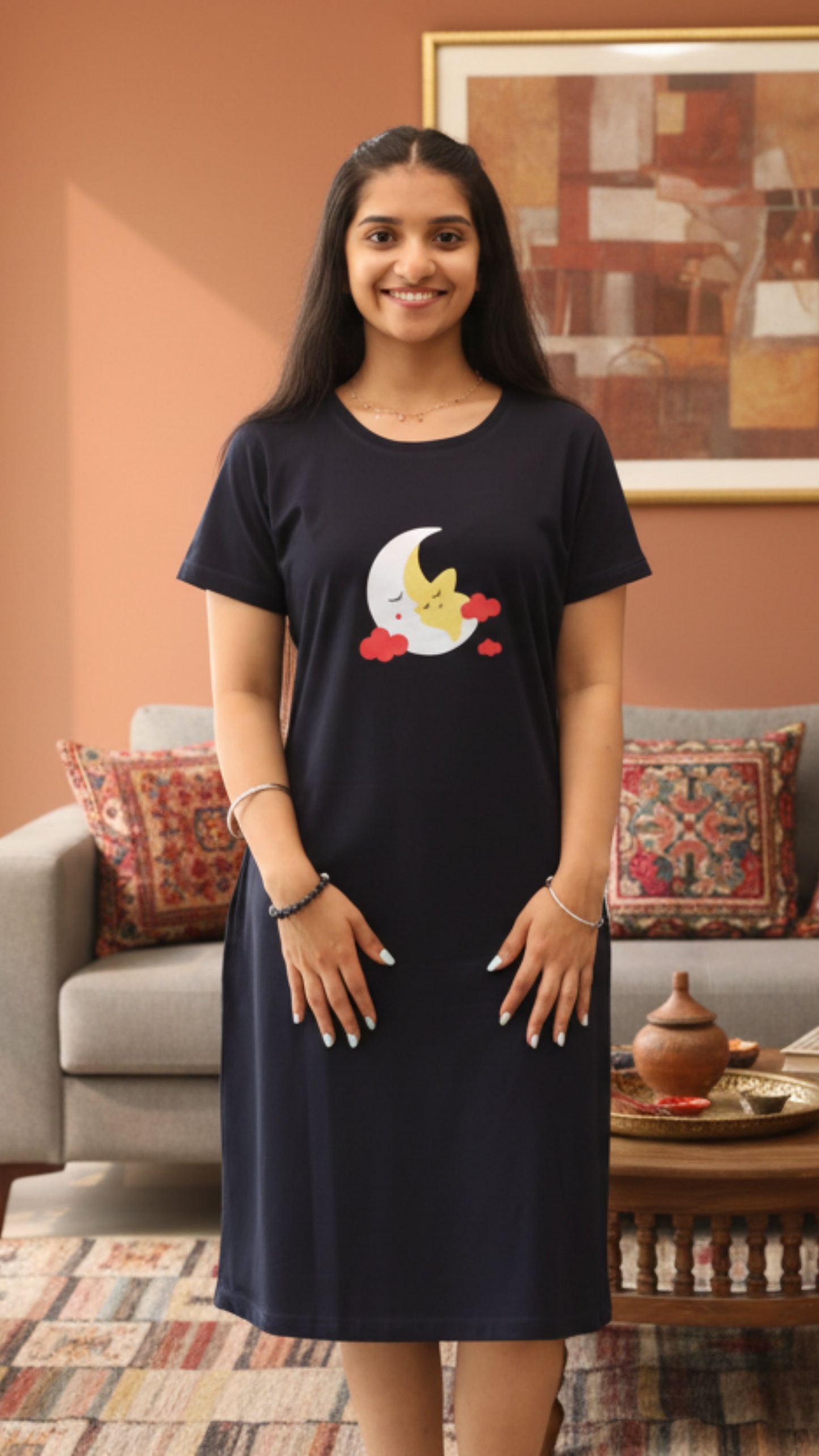 Woman wearing a dark navy cotton short nighty with a moon and star design in the chest area, standing in a living room.